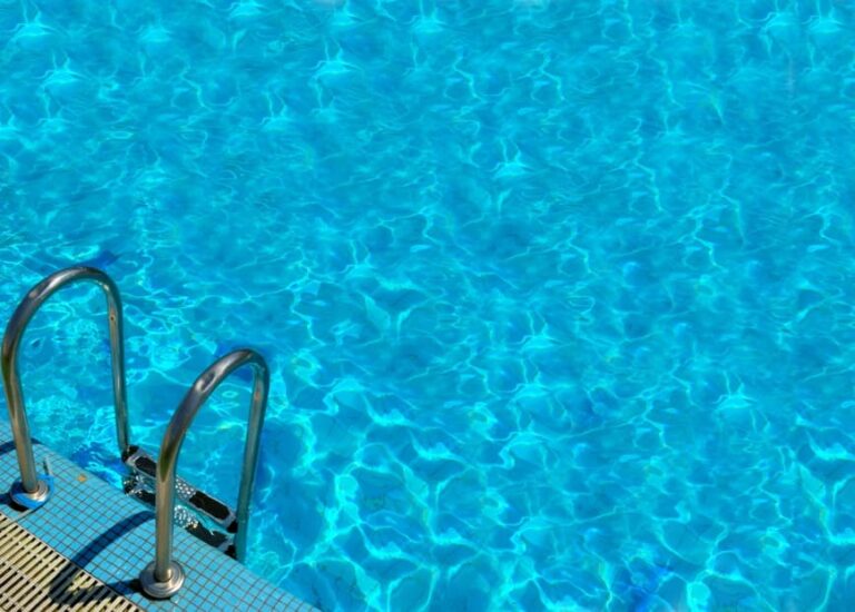 A stainless steel pool ladder leads into a clear blue swimming pool with rippling water, meticulously inspected to ensure electrical safety by an expert Vancouver electrician.