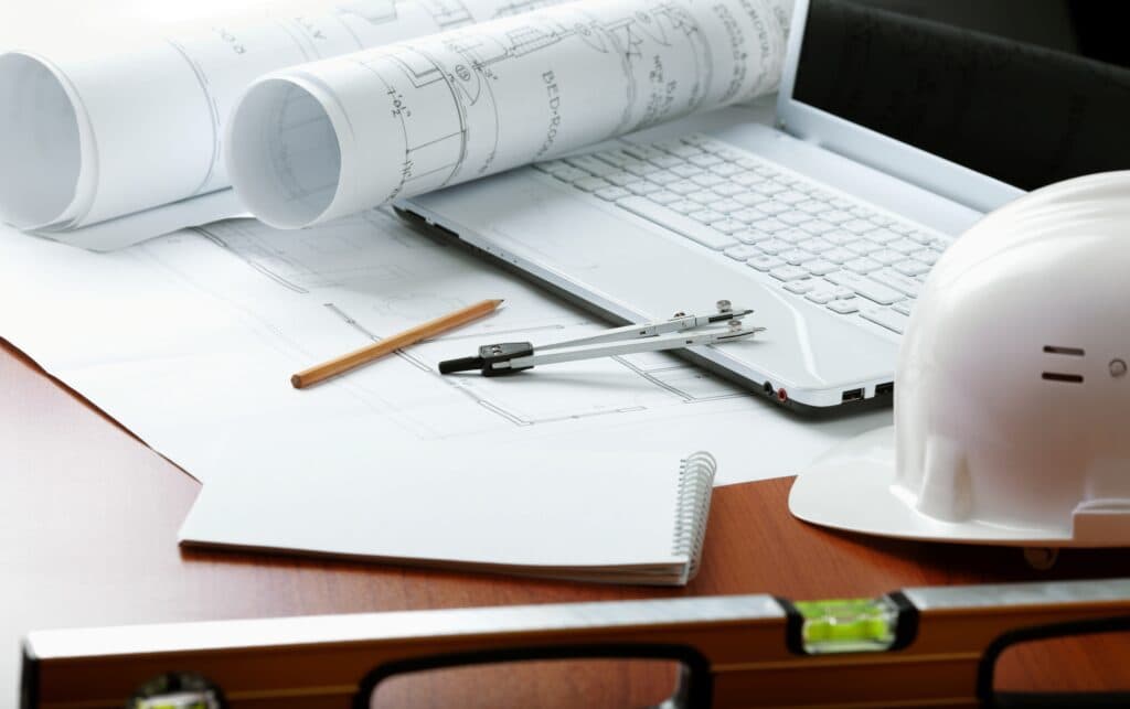 A desk in Vancouver, WA is equipped for an electrician's day of work, complete with a laptop, hard hat, and blueprints for their upcoming electrical service project. This workspace belongs to a local Vancouver electrician who is preparing to execute tasks efficiently and professionally.