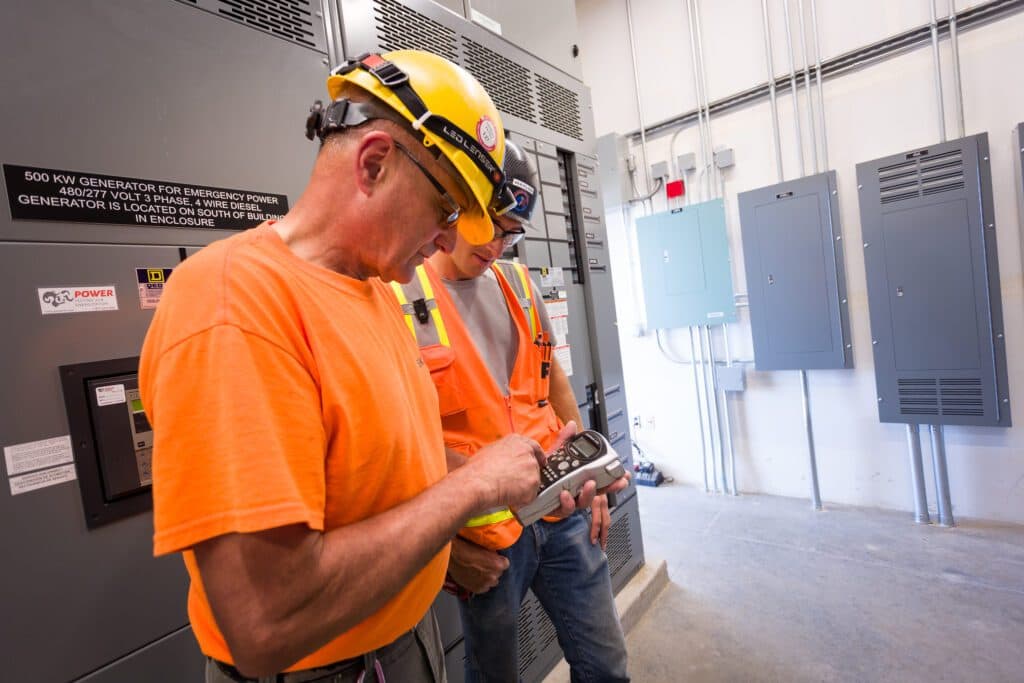 Two electricians from Vancouver, WA, one specializing in residential services and the other in commercial services, are positioned in front of an electrical panel.