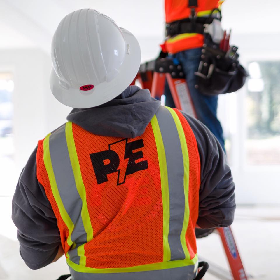 Prairie Electric electricians on a job site, one on a ladder in the background