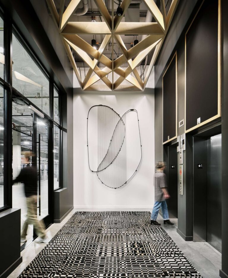 550 MLK in Portland, OR features a modern building lobby with advanced lighting and electrical solutions, supporting two elevators, dynamic lobby lighting for a geometric patterned floor and wooden lattice ceiling, and power for a large metal wall sculpture. Reliable electrician services ensure the smooth operation and maintenance of all electrical systems in this high-traffic space.