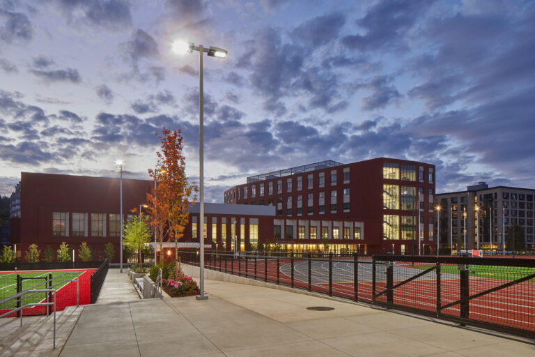 The image shows Lincoln High School's modern red-brick buildings illuminated at dusk in Vancouver, WA, with properly installed electrical lighting systems.