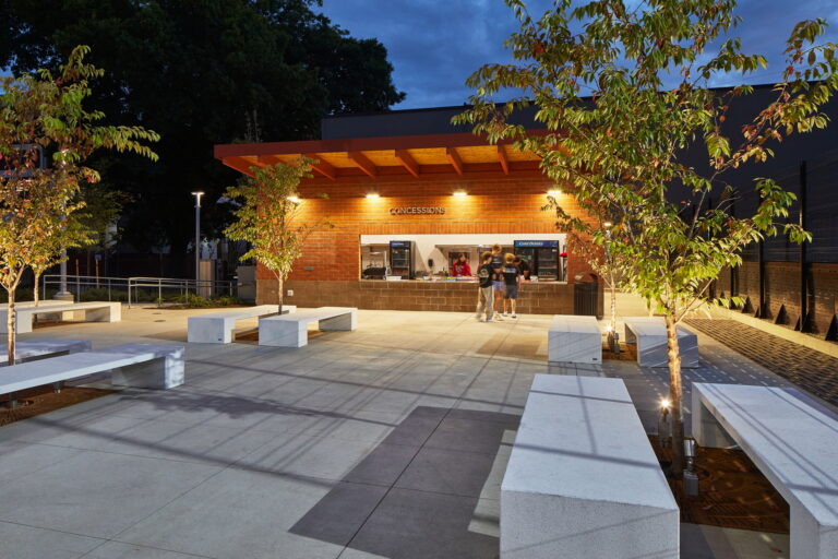 An evening concession stand near Lincoln High School, features modern outdoor lighting installed by professional electricians amidst paved walkways and white benches.