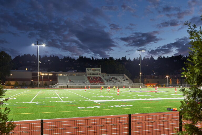 A well-lit sports field in Portland, OR hosts Lincoln High School players in red uniforms. Electricity powers this crucial night-time lighting for players and spectators, highlighting the importance of reliable local electrician services.