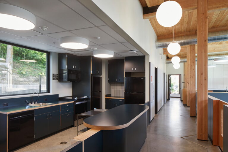 For electrician services in Vancouver, WA, consider installing modern kitchen lighting solutions. Large circular ceiling lights effectively illuminate spaces with black cabinets and countertops, ideal for a contemporary look reminiscent of a chic school cafeteria. Enhance your kitchen’s ambiance and functionality by contacting a local electrician today.