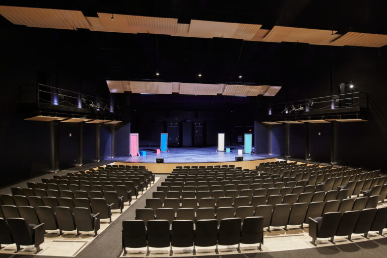 The large auditorium at Mountain View High School in Vancouver, WA is equipped with state-of-the-art electrician services. It features rows of seats facing a stage with simple props, soundproof panels on the ceiling, and specialized lighting that highlights the performance area.