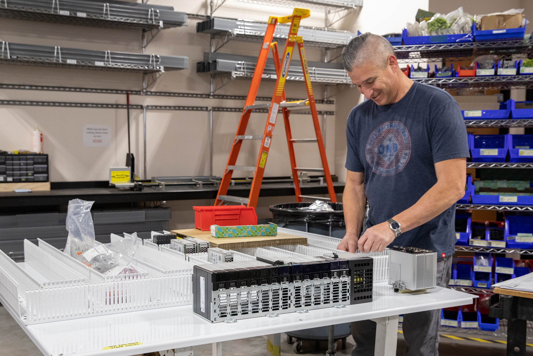 An electrician in Vancouver, WA works at a bench inspecting electronic components, surrounded by tools, supplies, and a red ladder.
