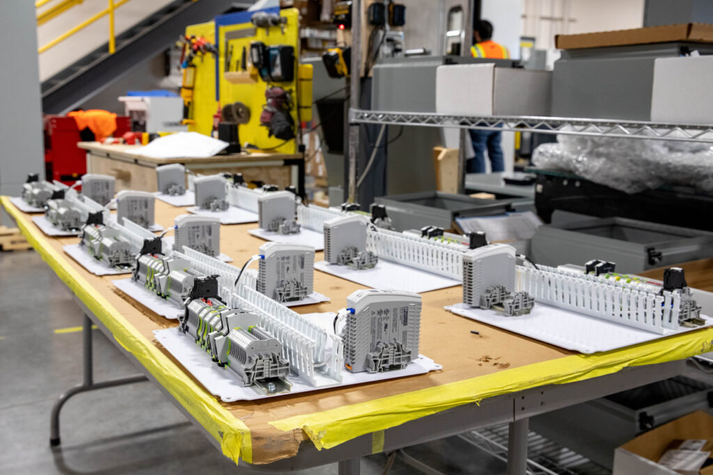Assembled electrical control panels are displayed on a workbench in an industrial warehouse in Vancouver, WA. Tools, equipment, shelves, and boxes are visible in the background—highlighting the electrician services available in the area.