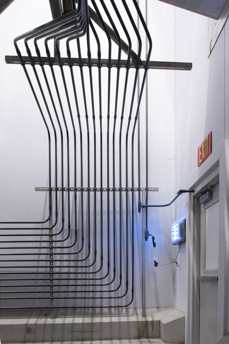 A series of black pipes and an exit sign are on a white wall showcasing sleek electrical work often found in upscale establishments. A tool with a blue light adds an intriguing touch next to a partially open door.