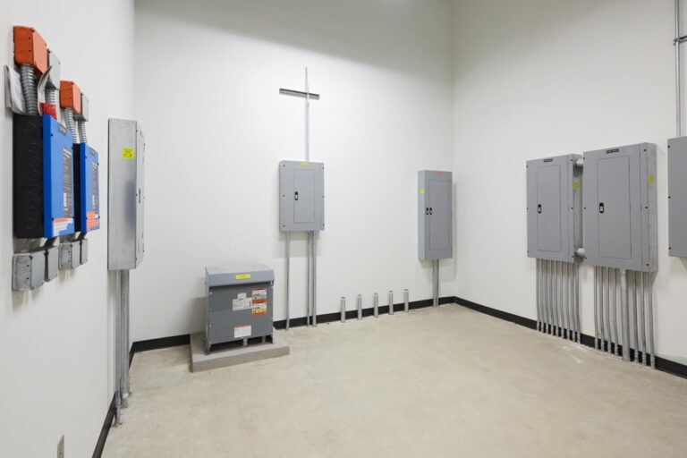 A room with electrical panels, a transformer box, and conduit tubing on the walls.