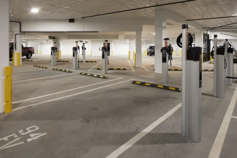 Indoor parking garage with multiple electric vehicle charging stations, each equipped with a charging cable. Several parking spaces are vacant, marked with yellow barriers.