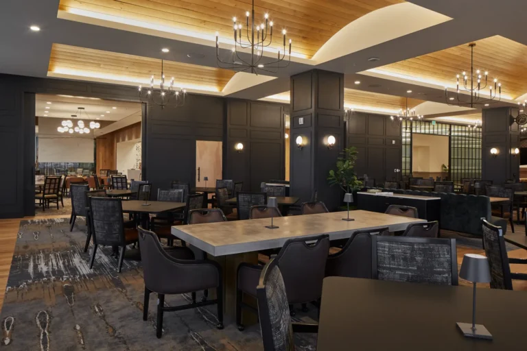 Spacious restaurant interior with modern decor, featuring wooden ceilings, chandeliers, dark-paneled walls, and neatly arranged tables and chairs.