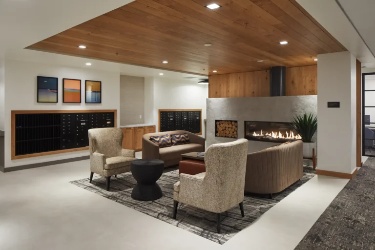 Contemporary lounge area with armchairs, a sofa, a circular table, and a fireplace. Wooden ceiling and flooring accents with wall art and potted plant.