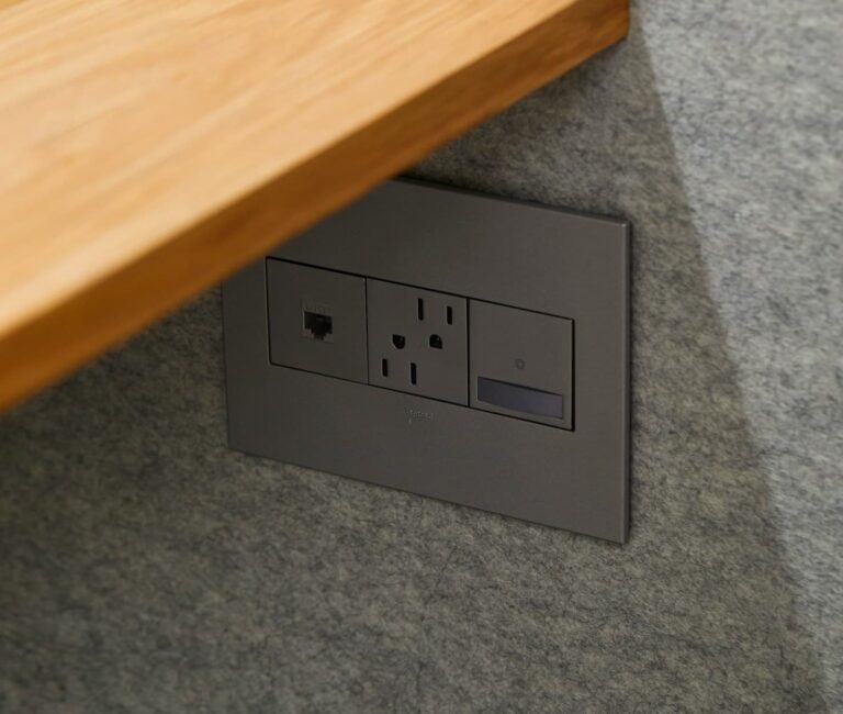 A gray wall-mounted outlet panel with a power outlet, phone jack, and USB port is expertly installed by a Vancouver electrician below a wooden shelf.