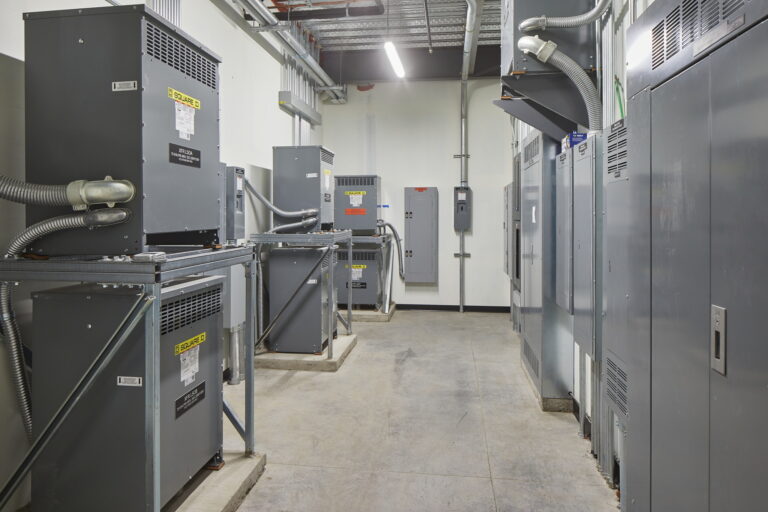 Large gray electrical cabinets and transformers. The neatly organized wires and labels highlight the professional electrical services available.