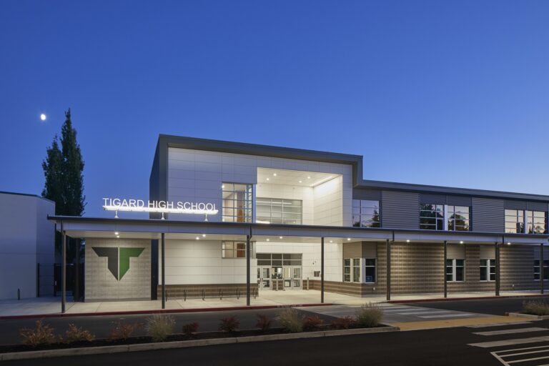 Tigard High School features a modern exterior with prominent lighting and large windows. The school's illuminated name and a well-lit pathway showcase expert electrician services.