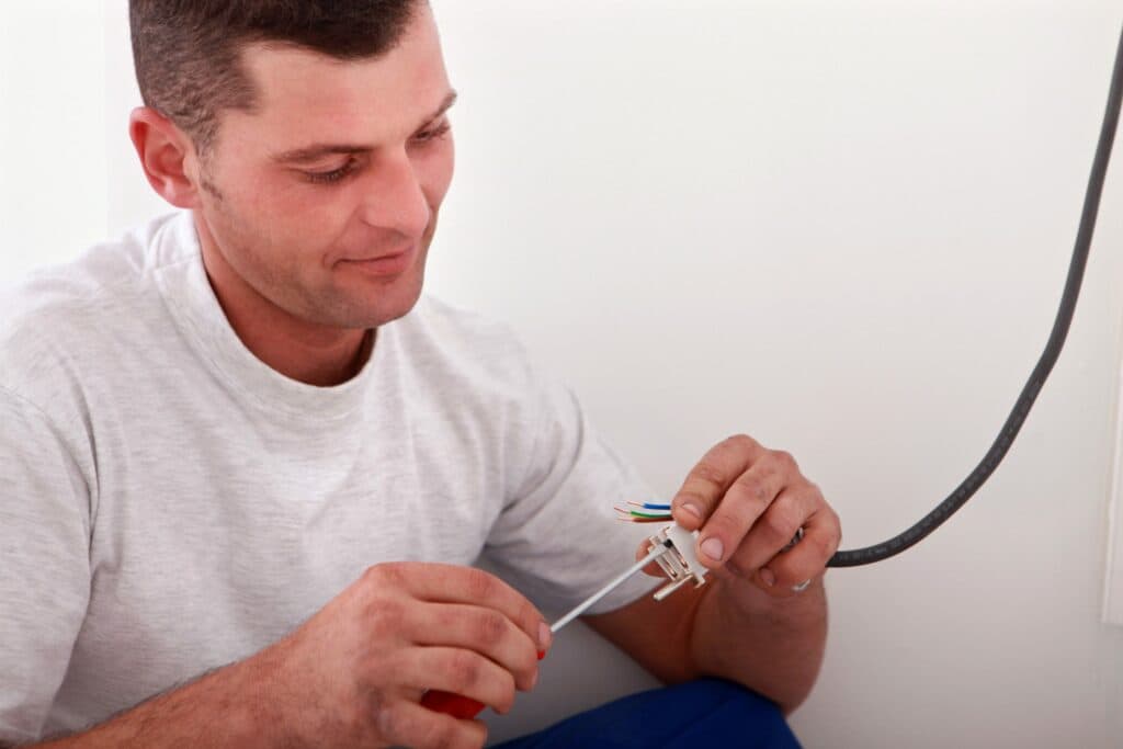 Electrician fitting plug to illustrate Add Outlet To Wall Leave it to the Professionals