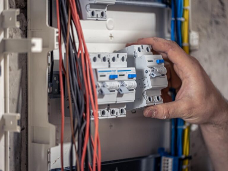 An electrician in Vancouver, WA adjusts circuit breakers inside an electrical panel with visible red, black, and yellow wiring.