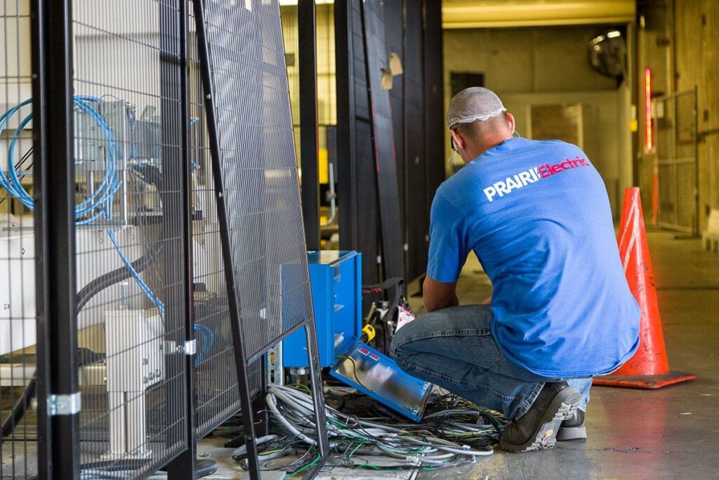 A local electrician in Vancouver, WA is seen taking a knee on the floor adjacent to some wires.