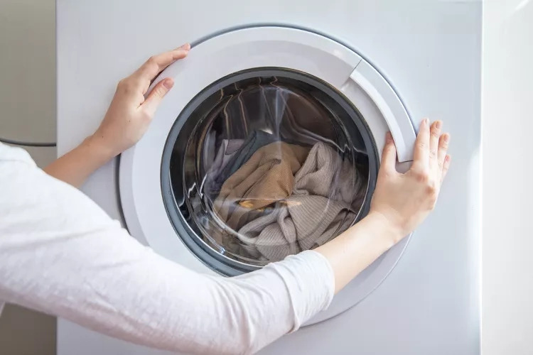 An electrician in Vancouver, WA inspects a front-loading washing machine, opening the door to check wiring and connections.
