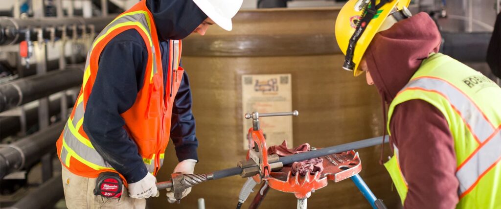 An electrician in a safety vest and white helmet is performing work with a pipe as part of residential electrical service in Vancouver, WA.