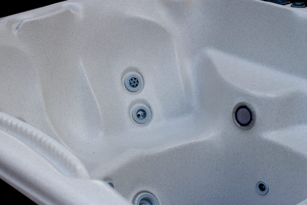Interior of an empty white hot tub with visible jets and drainage holes.