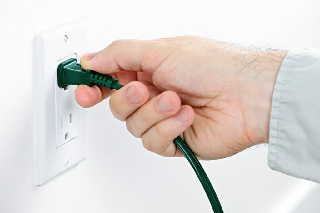 An electrician is connecting a green cord into a wall outlet for residential electrical services in Vancouver, WA.