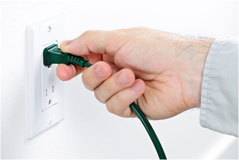 A hand, possibly that of a skilled Vancouver electrician, plugging a green electrical cord into a pristine white wall outlet.