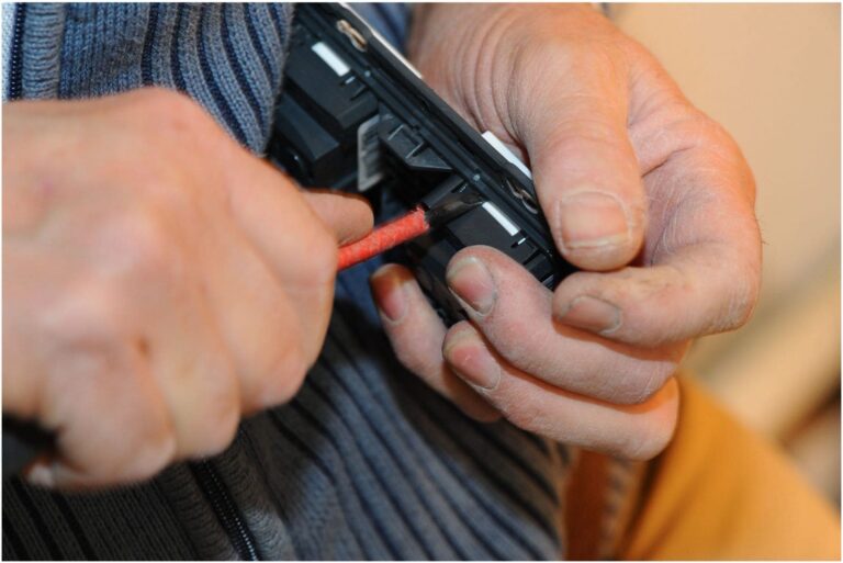 Hands of an electrician in Vancouver, WA, holding a tool, adjusting or repairing a device with a close-up focus on the activity.
