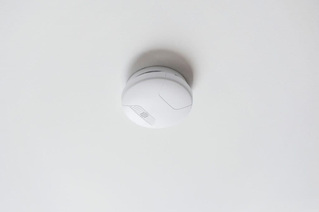 A white smoke alarm, for which a local electrician in Vancouver, WA can provide expert electrical service, is installed on the ceiling of a room by electricians.