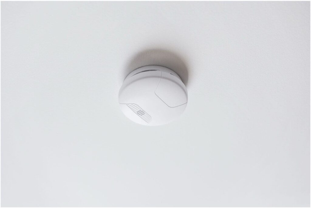 A white, circular smoke detector, installed by a Vancouver electrician, is mounted on the ceiling.