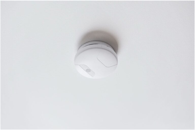 A white, circular smoke detector, installed by a Vancouver electrician, is mounted on the ceiling.