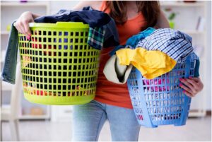 A person is carrying two laundry baskets filled with colorful clothes in a home setting, resembling the multitasking skills of an electrician in Vancouver, WA.