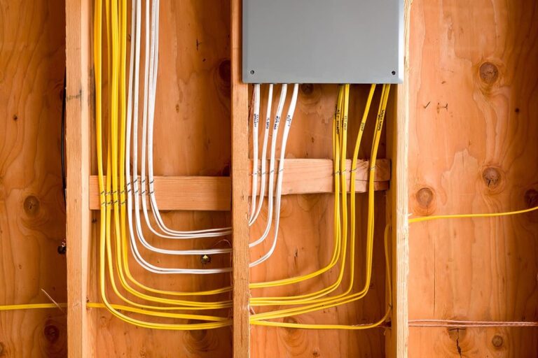 A group of yellow and white electrical wires run through the wooden framing of a wall, connected to a gray electrical box, skillfully installed by an electrician in Vancouver WA.