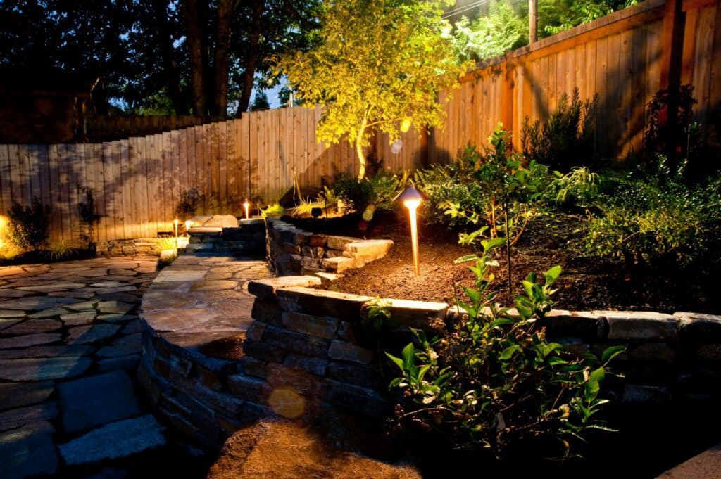 A backyard in Vancouver, WA is brilliantly lit up at night with a stone walkway cast in the warm glow of electric lighting installed by local electricians.