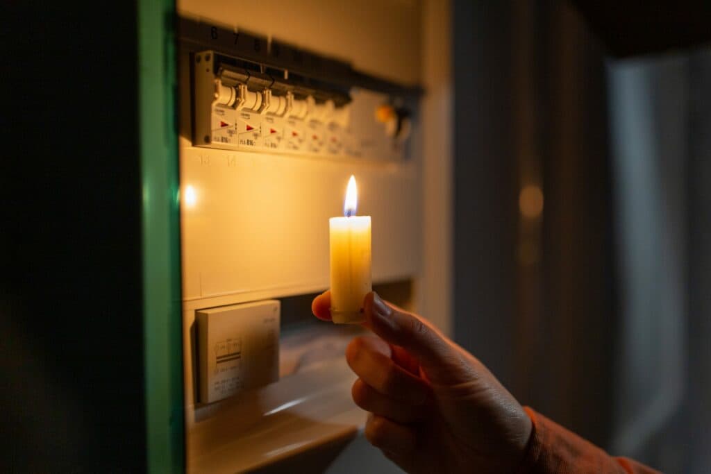 hand with burning candle near electric board to illustrate Power Went Out In Whole House