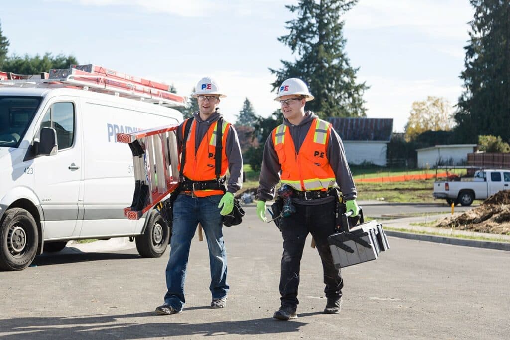Two electricians in safety vests and hardhats strolling down a street in Vancouver, WA.