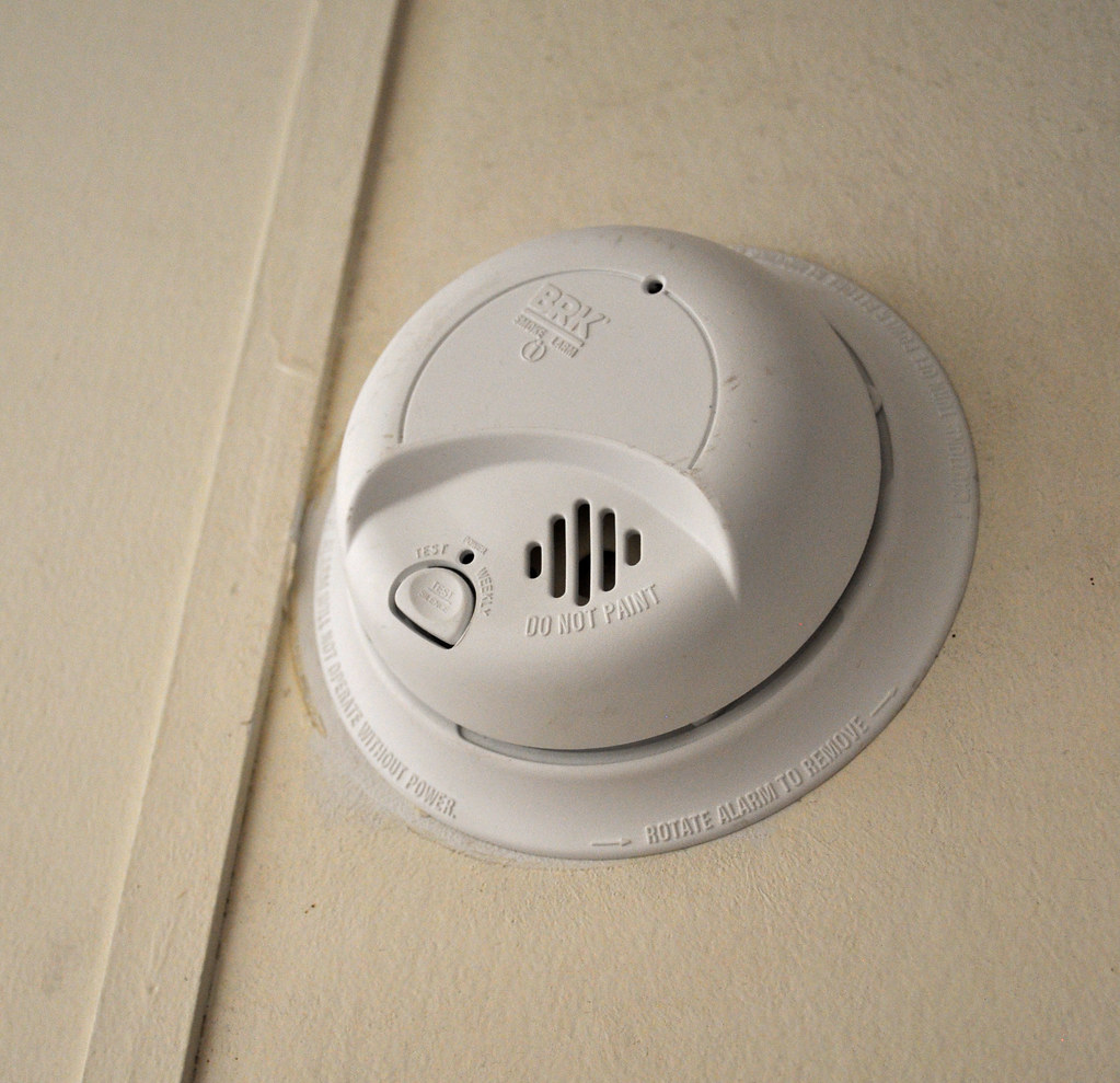 A white smoke detector with test button and safety labels is mounted on a ceiling in Vancouver, WA, ideal for electricians.