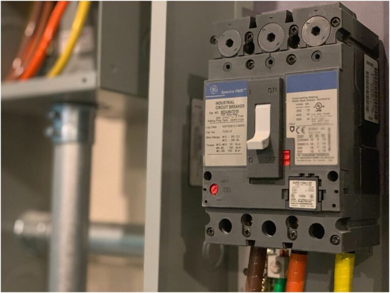 A close-up of an industrial circuit breaker in a gray electrical panel, installed by an electrician in Vancouver, WA, showcasing various colored wires and labels with technical information.